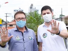 orvino e michel schlemper fazem o número cinco com as mãos para a foto; ambos usam máscara