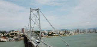 foto aérea da ponte hercílio luz com ônibus passando e continente ao fundo