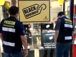 fiscais do procon municipal vistos de costas olhando para vitrine de relojoaria com placa "black november"