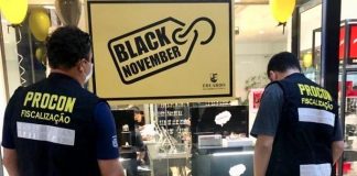 fiscais do procon municipal vistos de costas olhando para vitrine de relojoaria com placa "black november"