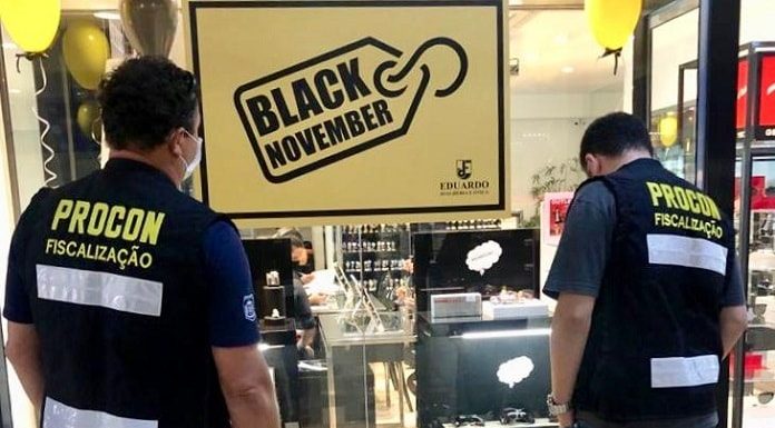 fiscais do procon municipal vistos de costas olhando para vitrine de relojoaria com placa "black november"