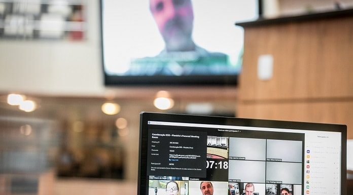 deputados vistos em transmissão em tela de notebook e outro deputado ao fundo em telão