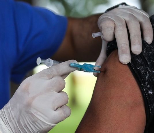vacinas: pessoa usando luva aplica dose de vacina em braço de uma senhora