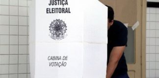 homem atrás de cabine de votação com o símbolo da justiça eleitoral