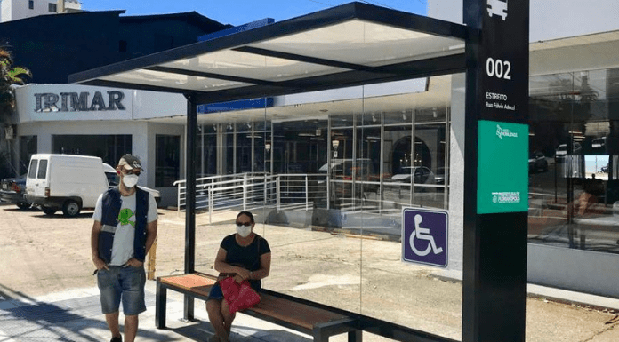 novos abrigos de passageiros: estrutura do Continente com cor verde, uma mulher sentada e um homem em pé aguardando o transporte coletivo
