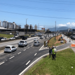aumentado o acesso da Via Expressa para a BR 101 - faixa nova de asfalto ao lado da rodovia, com homens no canteiro e carros passando