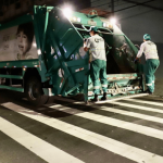 Dois homens na parte de trás de um caminhão de lixo verde em Florianópolis