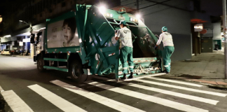 Dois homens na parte de trás de um caminhão de lixo verde em Florianópolis