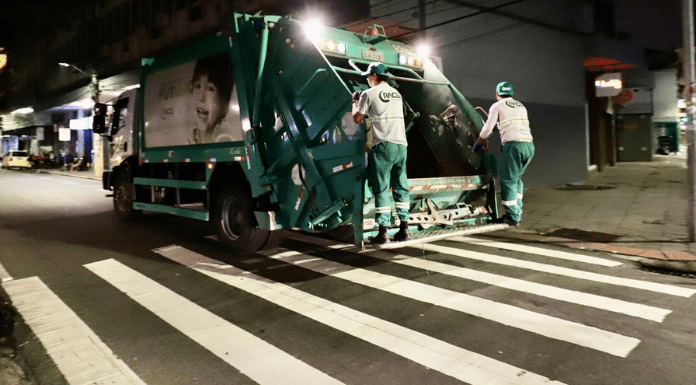 Dois homens na parte de trás de um caminhão de lixo verde em Florianópolis