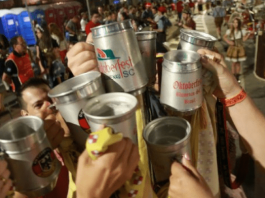 Várias pessoas com o braço levantado, brindando seus copos de cerveja em público