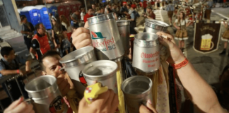 Várias pessoas com o braço levantado, brindando seus copos de cerveja em público
