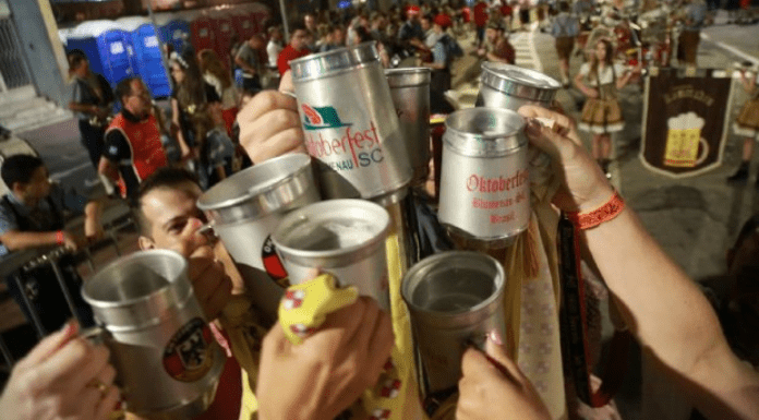 Várias pessoas com o braço levantado, brindando seus copos de cerveja em público