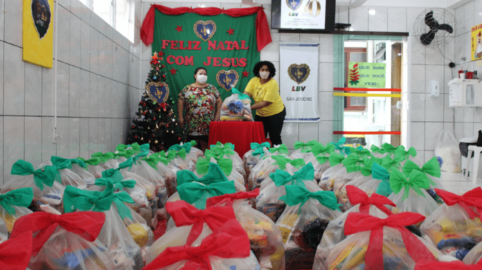 Sacos com alimentos e kits de limpeza com laços natalinos nas cores: vermelho e verde