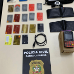 Cartões de crédito clonados, carteiras, celulares e uma placa da Polícia Civil de Santa Catarina em cima da mesa