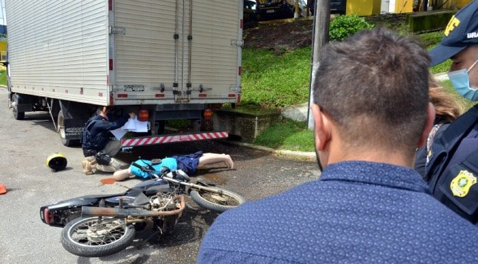 para conscientizar motociclistas: homem olha moto e boneco caídos atrás de caminhão, com prf ao lado