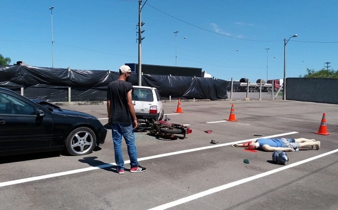 homem olha boneco caído na frente de um carro simulando acidente de moto