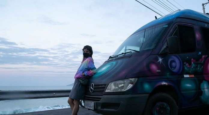 Thais Alemany encostada em uma van na estrada em frente ao mar