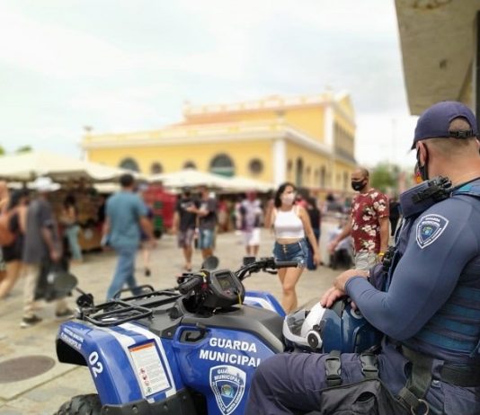 guarda municipal de florianópolis em fiscalização olha para movimentação de pessoas no largo da alfândega na semana de natal; ele está sentado em um quadriciclo