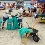 dois garis da comcap fazem coleta de lixo nas praias de florianópolis, na imagem na praia do campeche; guarda-sóis em volta