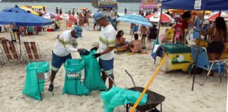 dois garis da comcap fazem coleta de lixo nas praias de florianópolis, na imagem na praia do campeche; guarda-sóis em volta