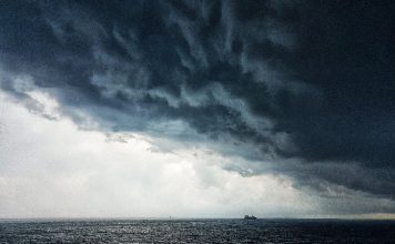 Defesa Civil alerta para tempestade na região sul do brasil - nuvem carregada sobre o oceano, com pequena embarcação no horizonte