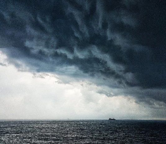 Defesa Civil alerta para tempestade na região sul do brasil - nuvem carregada sobre o oceano, com pequena embarcação no horizonte