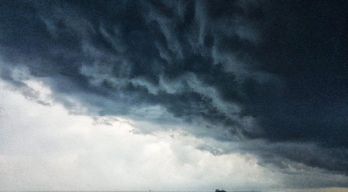 alerta de tempestade no sábado (19/12) para região sul do brasil - nuvem carregada sobre o oceano, com pequena embarcação no horizonte