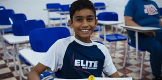 Menino em sala de aula do Elite Rede de Ensino, com uniforme da instituição e com o caderno aberto em cima da mesa