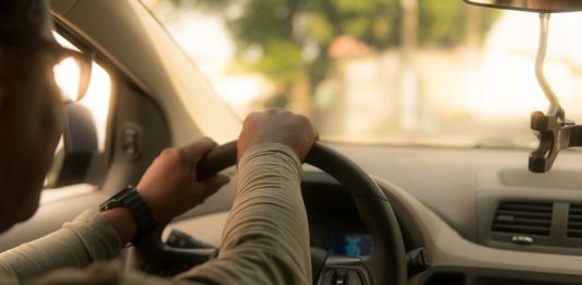 emprego uber: motorista é visto pelo ângulo do banco de trás dirigindo o carro; ele usa óculos