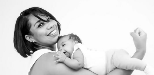 Bebês e suas mães - mãe sorri para a câmera com o bebê apoiado ao longo do braços