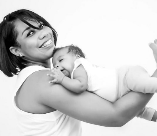 Bebês e suas mães - mãe sorri para a câmera com o bebê apoiado ao longo do braços