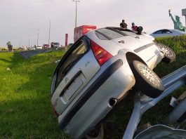 citroen virado de lado no gramado ao lado da via expressa; placa censurada