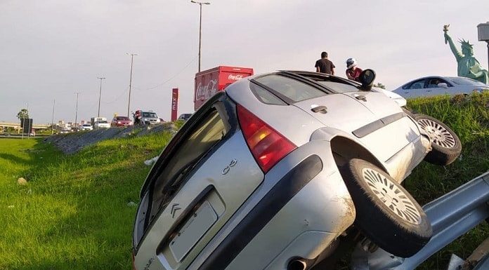 citroen virado de lado no gramado ao lado da via expressa; placa censurada