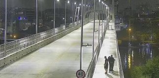 decreto do toque de recolher em sc: ponte hercílio luz à noite, com três pessoas andando na passarela