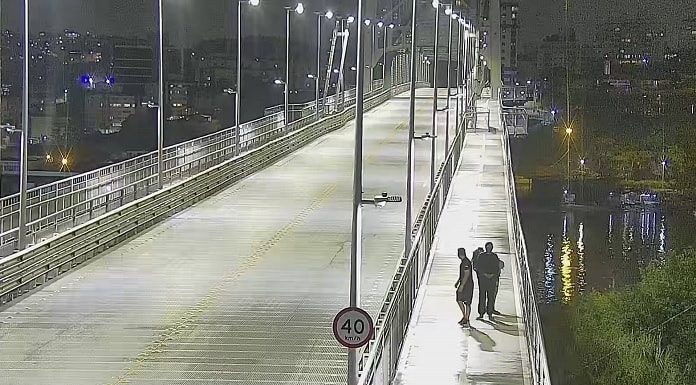 decreto do toque de recolher em sc: ponte hercílio luz à noite, com três pessoas andando na passarela