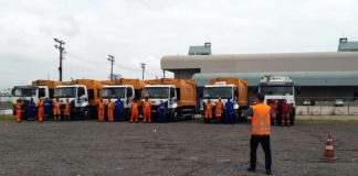 equipes em frente a cinco caminhões laranjas de lixo estacionados em pátio ao lado do centro sul