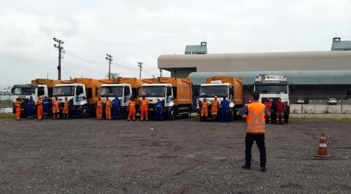 equipes em frente a cinco caminhões laranjas de lixo estacionados em pátio ao lado do centro sul