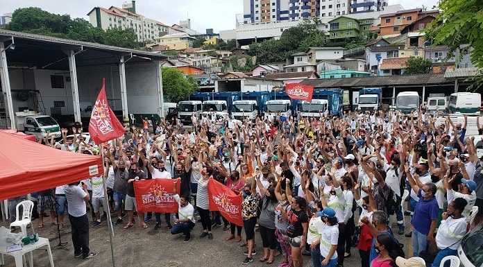 termina a greve da comcap com acordo de reajuste; centenas de pessoas reunidas em pátio da companhia; muitas com os braços para cima; tenda do sindicato à frente; caminhões ao fundo