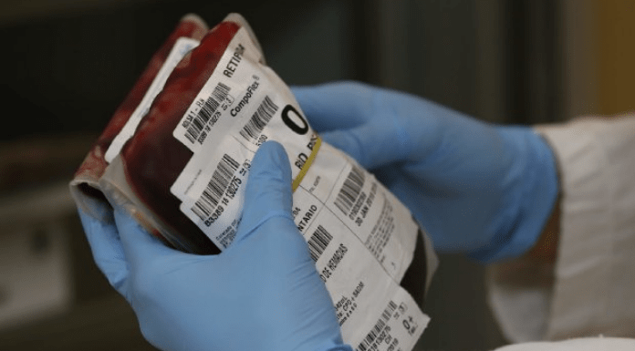 Zoom nas mãos de uma pessoa com luvas azuis segurando uma pacote de doação de sangue