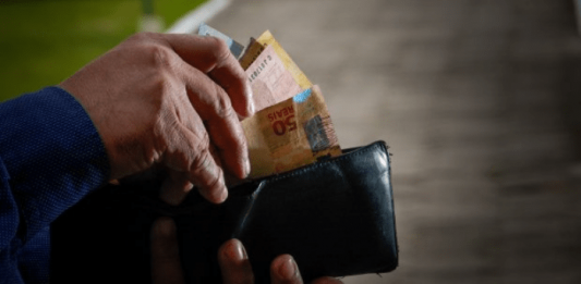 Prática abusiva do Banco C6 com clientes: Pessoa mexendo na carteira e tirando cédulas de dinheiro