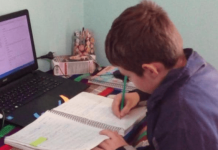 Criança em casa, com notebook em sua frente e escrevendo em um caderno