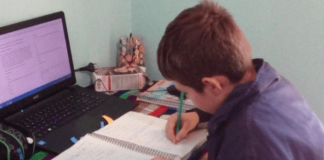 Criança em casa, com notebook em sua frente e escrevendo em um caderno