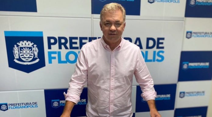 gean posa para a foto com os chips de celulares para os estudantes de florianópolis; painel da prefeitura ao fundo