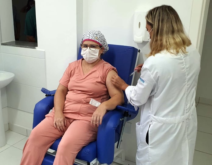 profissional de saúde sendo vacinada no braço sentada em poltrona em consultório