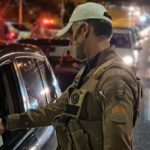 policial militar usa máscara e faz teste de bafômetro em motorista; grande trânsito ao fundo - motoristas foram flagrados embriagados