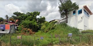 frente de um dos imóveis da comcap que pode ir a leilão; terreno baldio com cerca na frente e casas ao lado