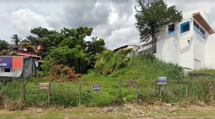 frente de um dos imóveis da comcap que pode ir a leilão; terreno baldio com cerca na frente e casas ao lado