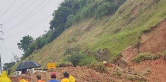 funcionários com capas de chuva olhando par monte de terra sobre rodovia ao lado de grande barranco - via expressa interditada por deslizamento