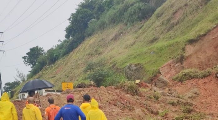 funcionários com capas de chuva olhando par monte de terra sobre rodovia ao lado de grande barranco - via expressa interditada por deslizamento