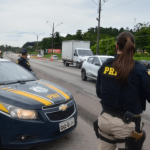 Policial de costas ao lado do carro da PRF na rodovia